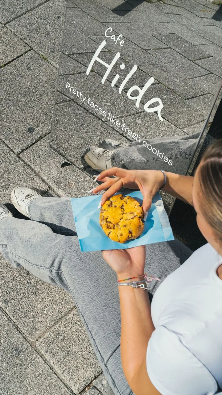 Gast sitzt mit einem Cookie vor dem Café-Hilda-Schild